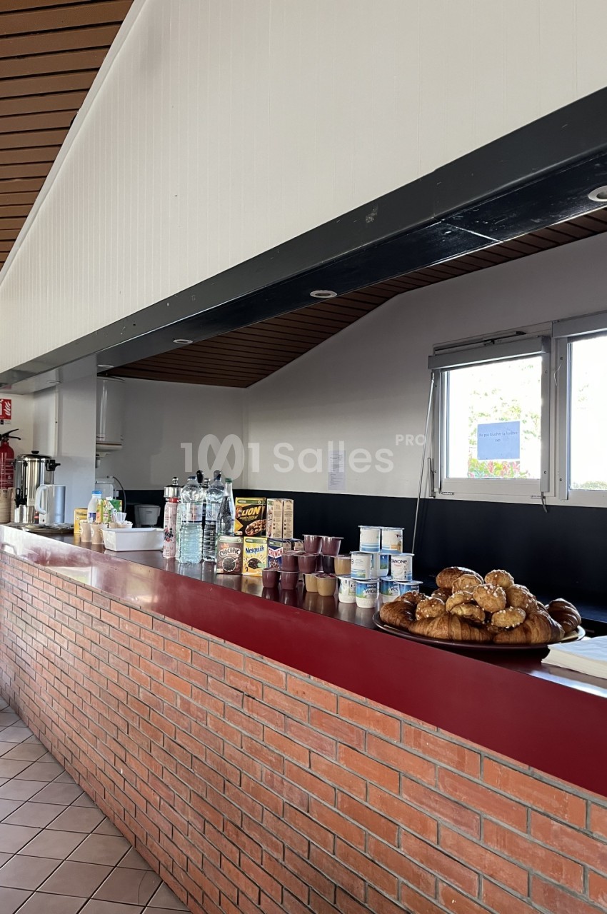 Comptoir en briques avec viennoiseries, boissons et produits alimentaires exposés dans une salle lumineuse.