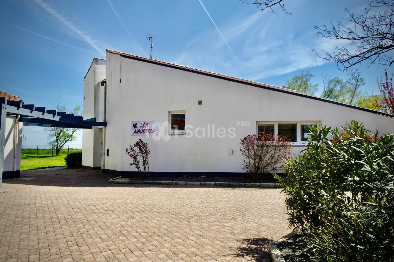 Bâtiment blanc moderne avec un toit incliné, entouré de végétation et d'un chemin pavé sous un ciel dégagé.