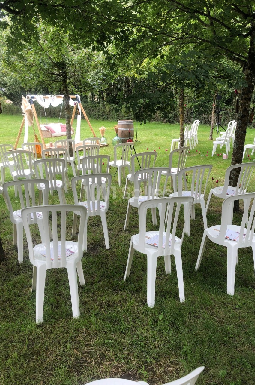 Chaises blanches en plastique disposées en rangées sur une pelouse, face à une arche décorée pour une cérémonie en plein air.