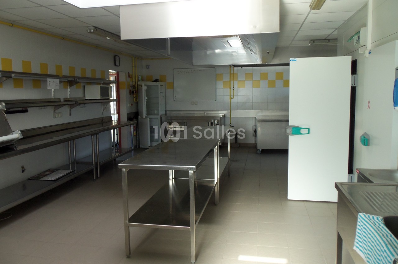 Cuisine professionnelle avec plans de travail en inox, carrelage mural blanc et jaune, et équipements de restauration.