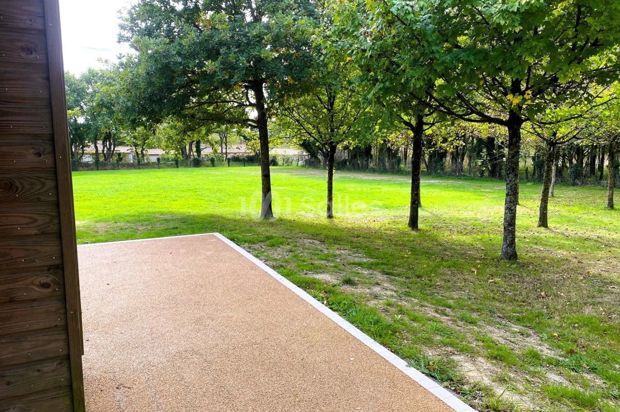 Allée en gravier beige bordée d'herbe, donnant sur un espace vert avec des arbres sous un ciel clair.