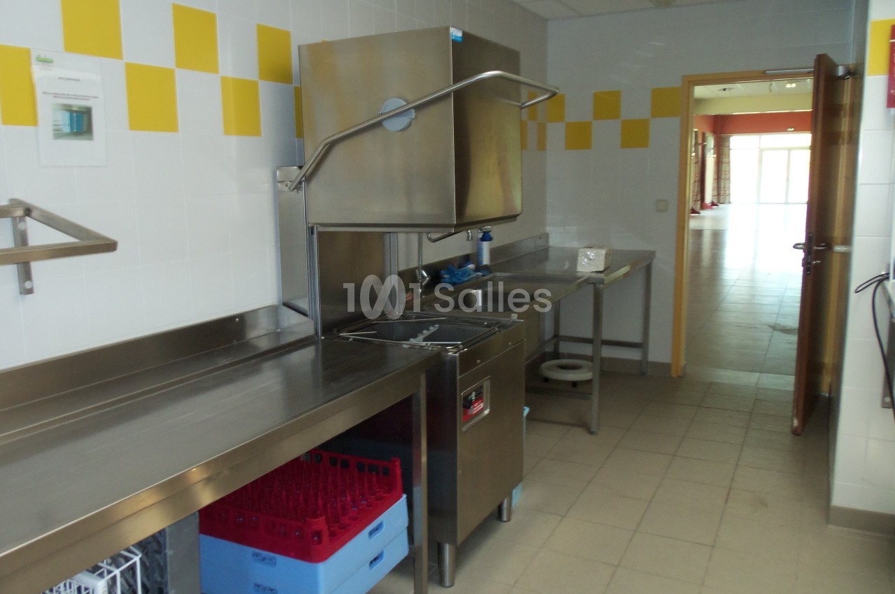Cuisine professionnelle avec plan de travail en inox, lave-vaisselle industriel et casiers de rangement colorés.