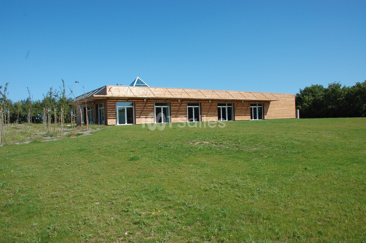 Bâtiment en bois à un étage avec de grandes baies vitrées, entouré d'une pelouse et d'arbres sous un ciel bleu.