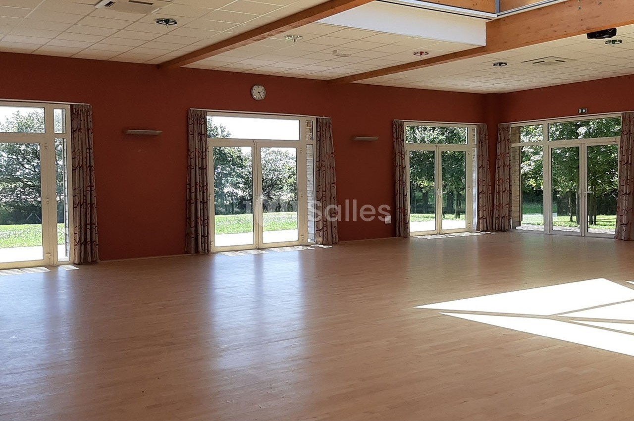 Salle lumineuse avec parquet clair, grandes baies vitrées donnant sur un espace extérieur verdoyant.