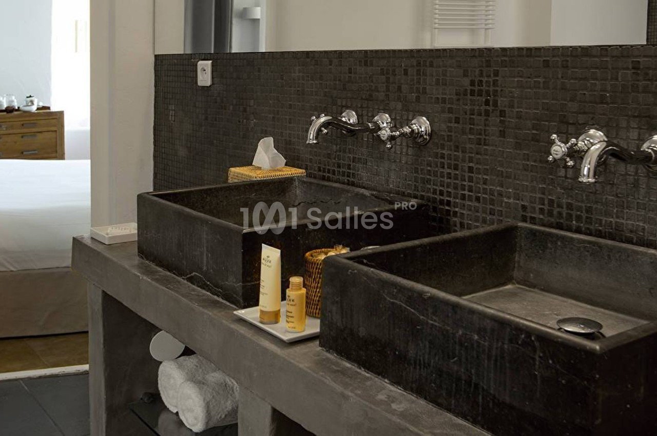 Deux lavabos noirs en pierre avec robinetterie murale, posés sur un plan en béton, dans une salle de bain moderne.