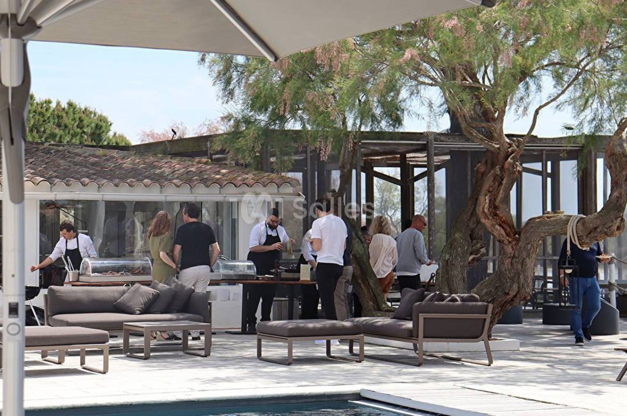 Personnes réunies autour d'un buffet en extérieur près d'une piscine, avec des meubles de jardin et des arbres en arrière…