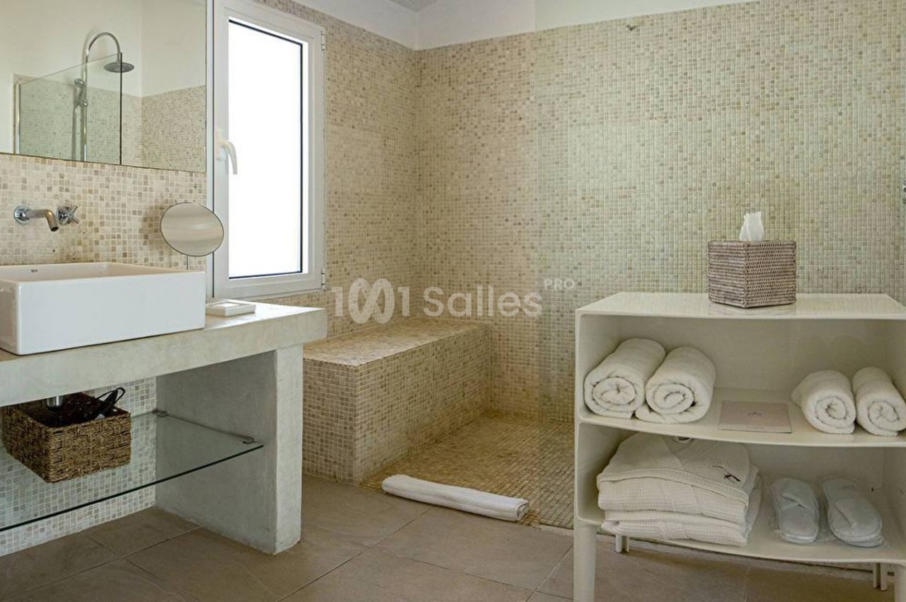 Salle de bain moderne avec douche à l'italienne, vasque sur plan en béton, étagère avec serviettes pliées et fenêtre.