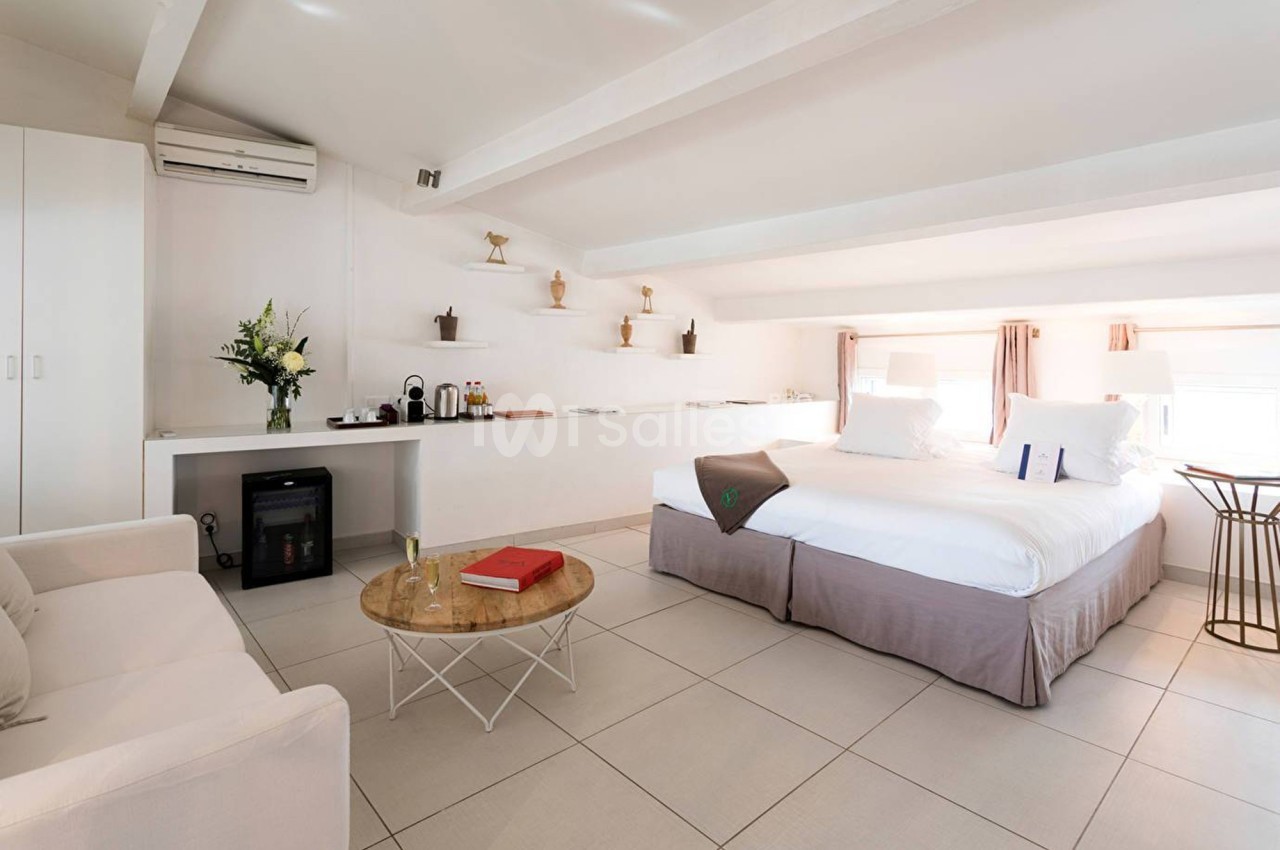 Chambre lumineuse avec lit double, canapé, table basse, kitchenette équipée et décoration minimaliste.