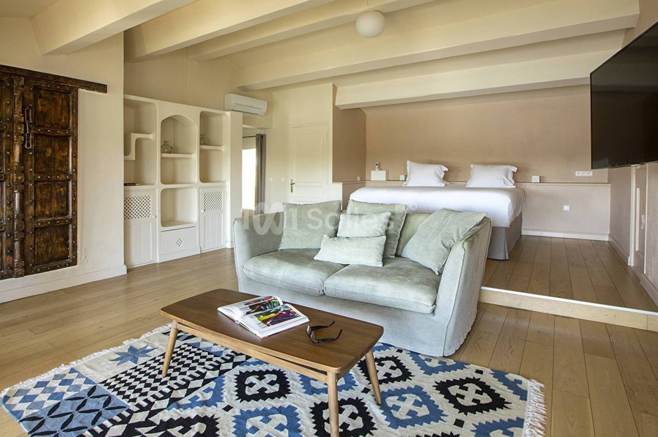 Salon lumineux avec canapé, table basse, tapis à motifs, et chambre en mezzanine avec lit double en arrière-plan.