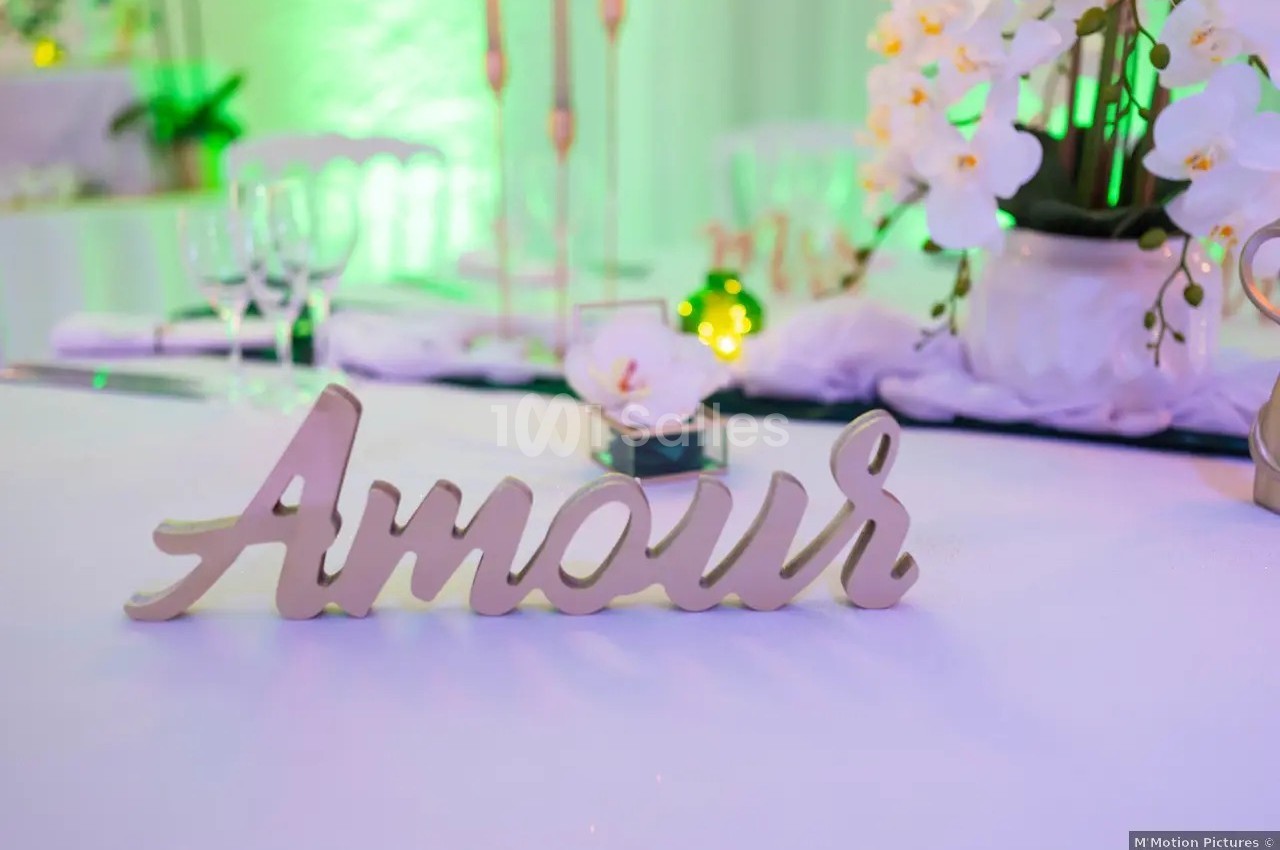 Décoration de table avec le mot ’Amour’ en bois, des fleurs blanches et une ambiance lumineuse verte.