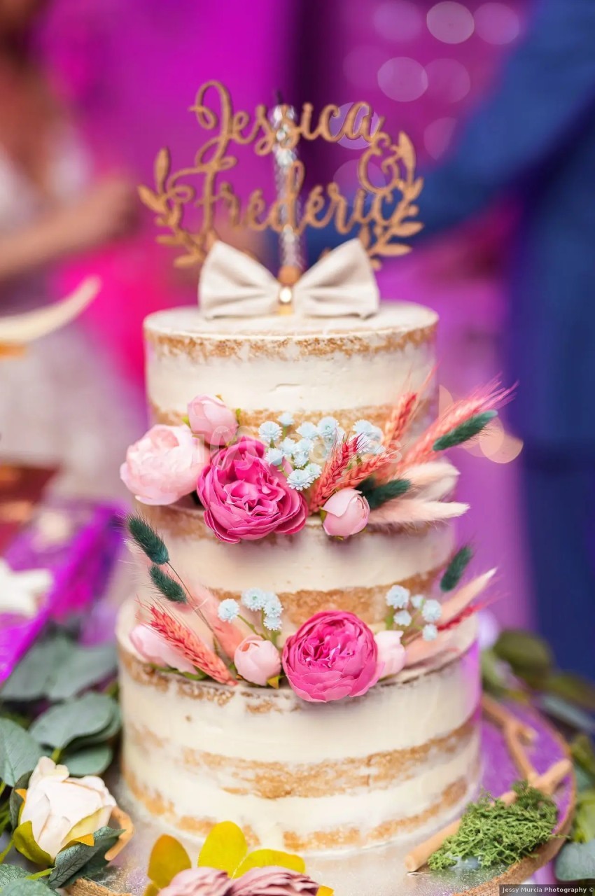 Gâteau de mariage à trois étages décoré de fleurs roses et séchées, avec un topper portant des prénoms.