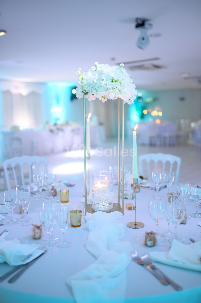 Table de réception élégamment dressée avec un centre de table floral blanc, bougies et vaisselle raffinée.