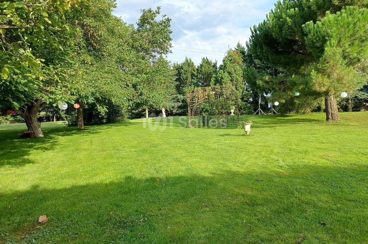 Pelouse verdoyante avec des arbres, une arche décorative et des lanternes suspendues dans un jardin ensoleillé.