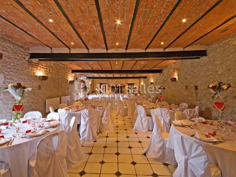 Salle de réception avec murs en pierre, plafond en briques et tables décorées pour un événement festif.
