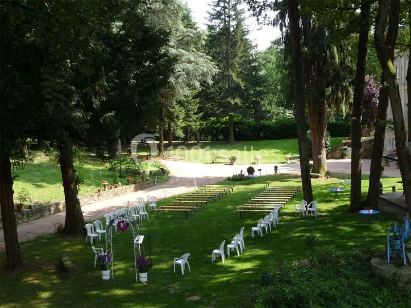 Chaises blanches et bancs disposés en extérieur sur une pelouse, entourés d'arbres, préparés pour un événement.