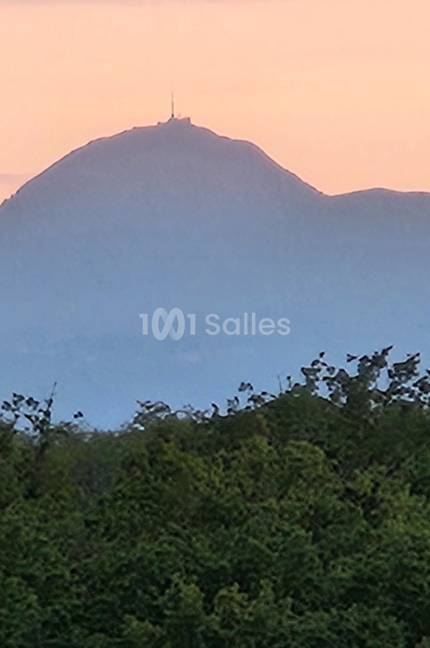 Vue d'un sommet montagneux au coucher du soleil, avec des arbres au premier plan et un ciel teinté de rose.