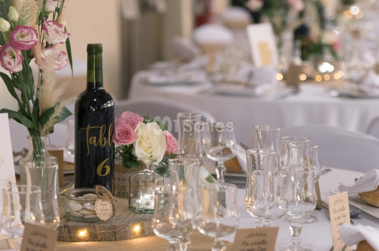 Table décorée pour un événement avec fleurs, bougies, bouteille de vin marquée ’Table 6’ et vaisselle élégante.