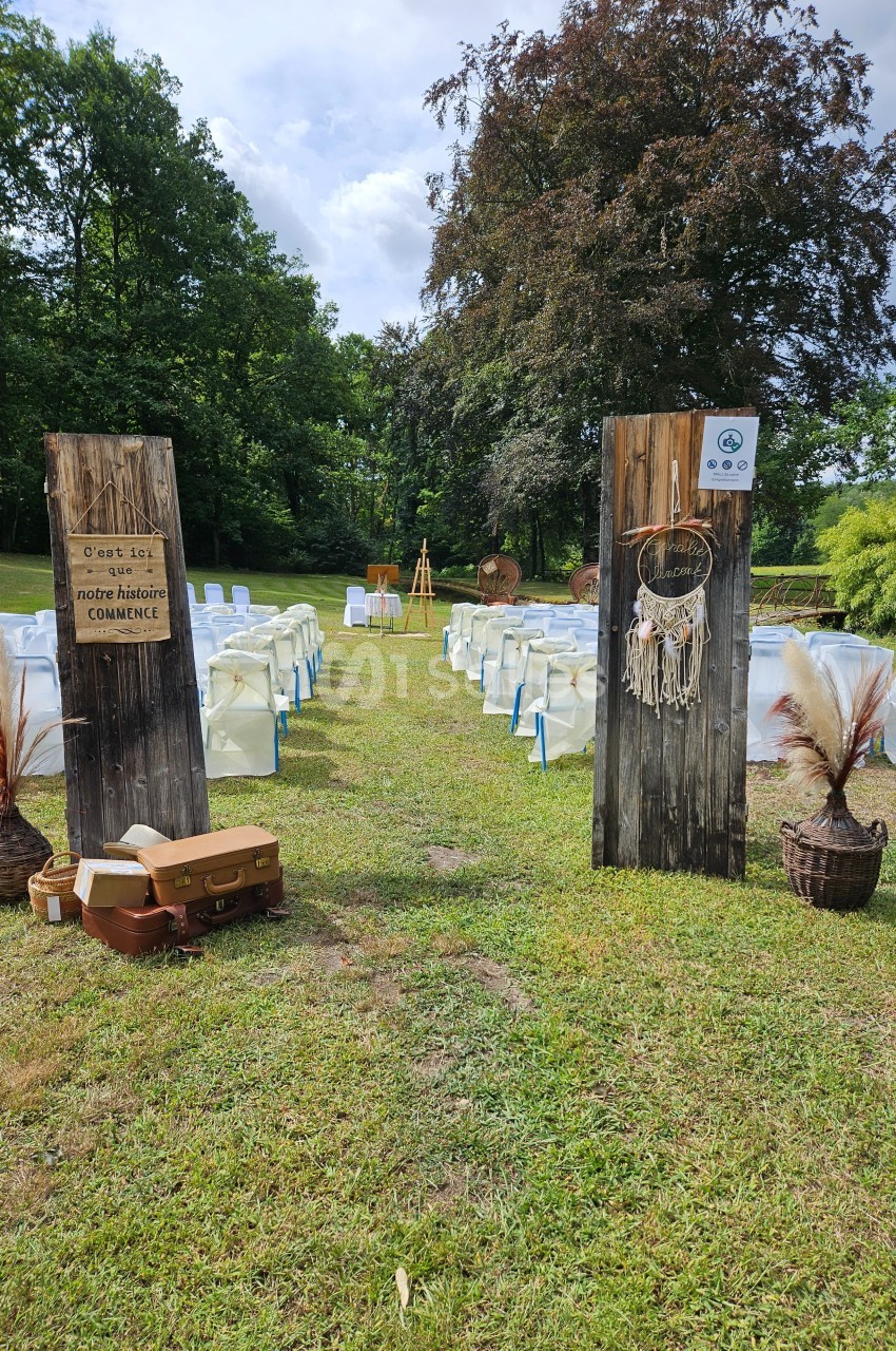 Allée centrale d'une cérémonie en plein air avec des chaises alignées, des panneaux en bois et des décorations bohèmes.