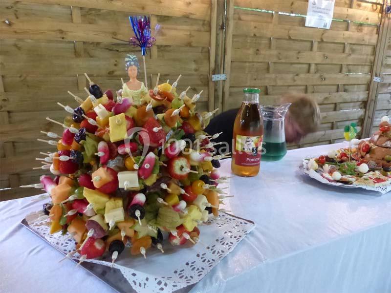 Brochettes de fruits variés disposées en forme de bouquet sur une table, avec une bouteille et une carafe en arrière-plan.