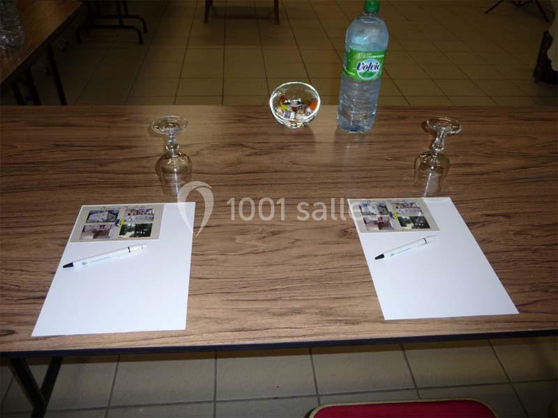 Deux places de réunion avec feuilles, stylos, verres vides et une bouteille d'eau sur une table en bois.