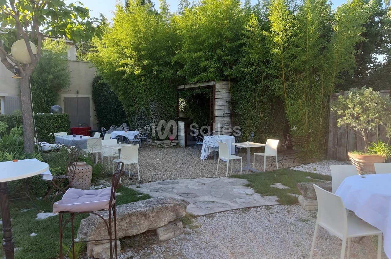 Jardin avec tables et chaises blanches disposées sur du gravier, entouré de bambous et de verdure.