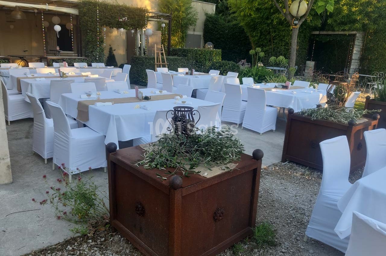 Tables et chaises blanches disposées en extérieur pour un événement, entourées de verdure et de décorations simples.