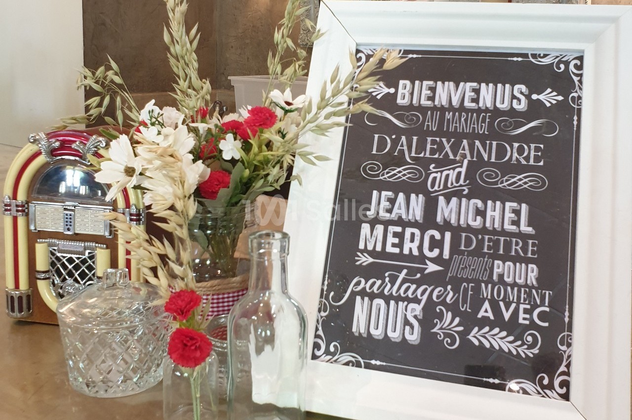 Panneau de bienvenue pour un mariage, entouré de fleurs, d'un jukebox et de carafes en verre sur une table.