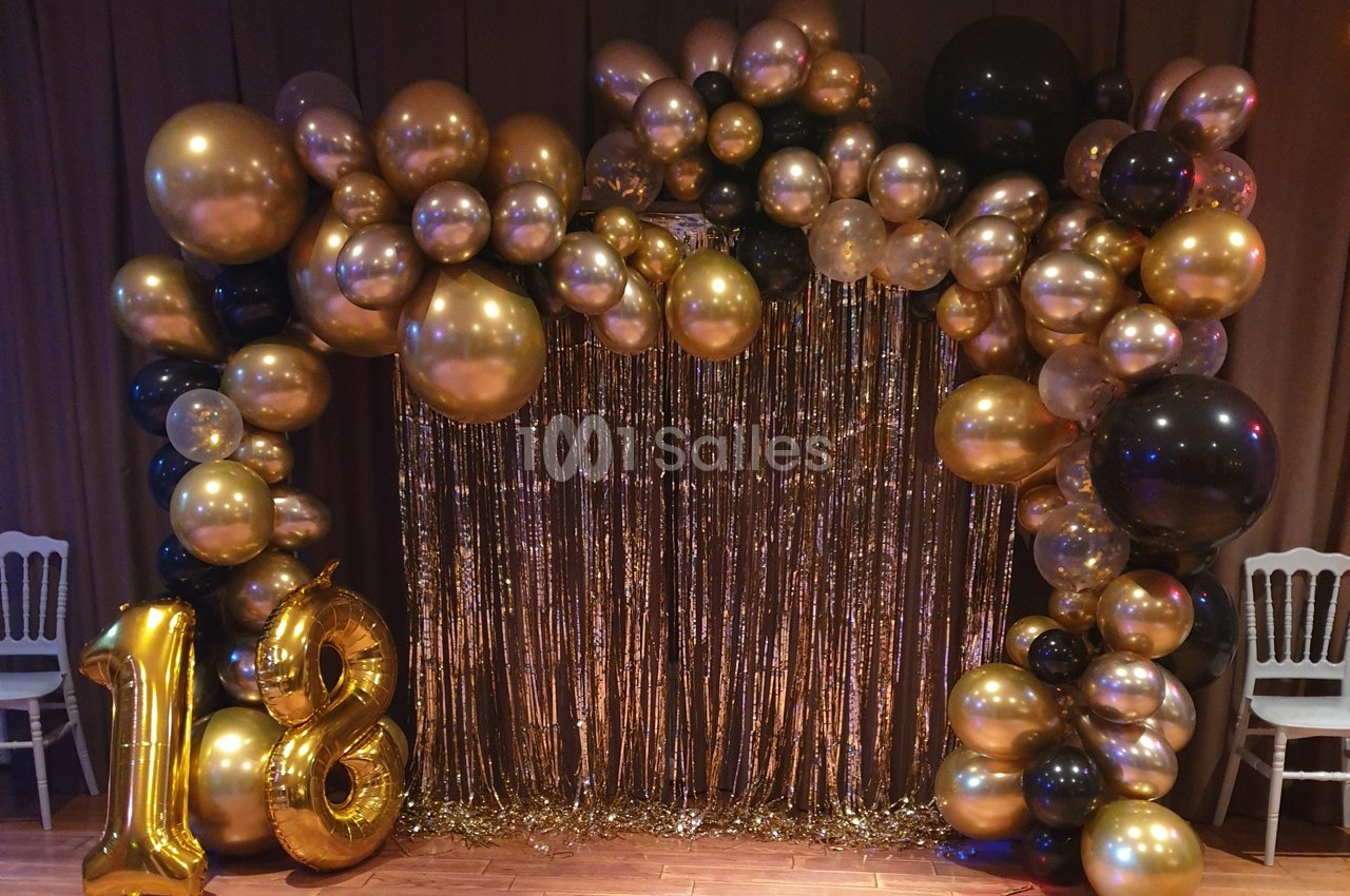 Décoration festive avec arche de ballons dorés et noirs, rideau scintillant et ballons formant le chiffre 18.