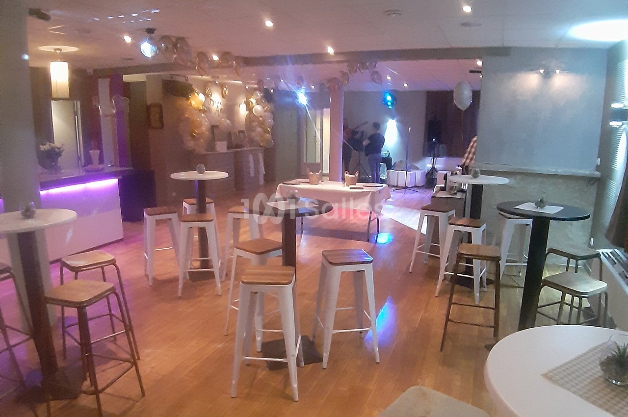 Salle de réception avec tables hautes, tabourets et éclairage tamisé, décorée pour un événement festif.