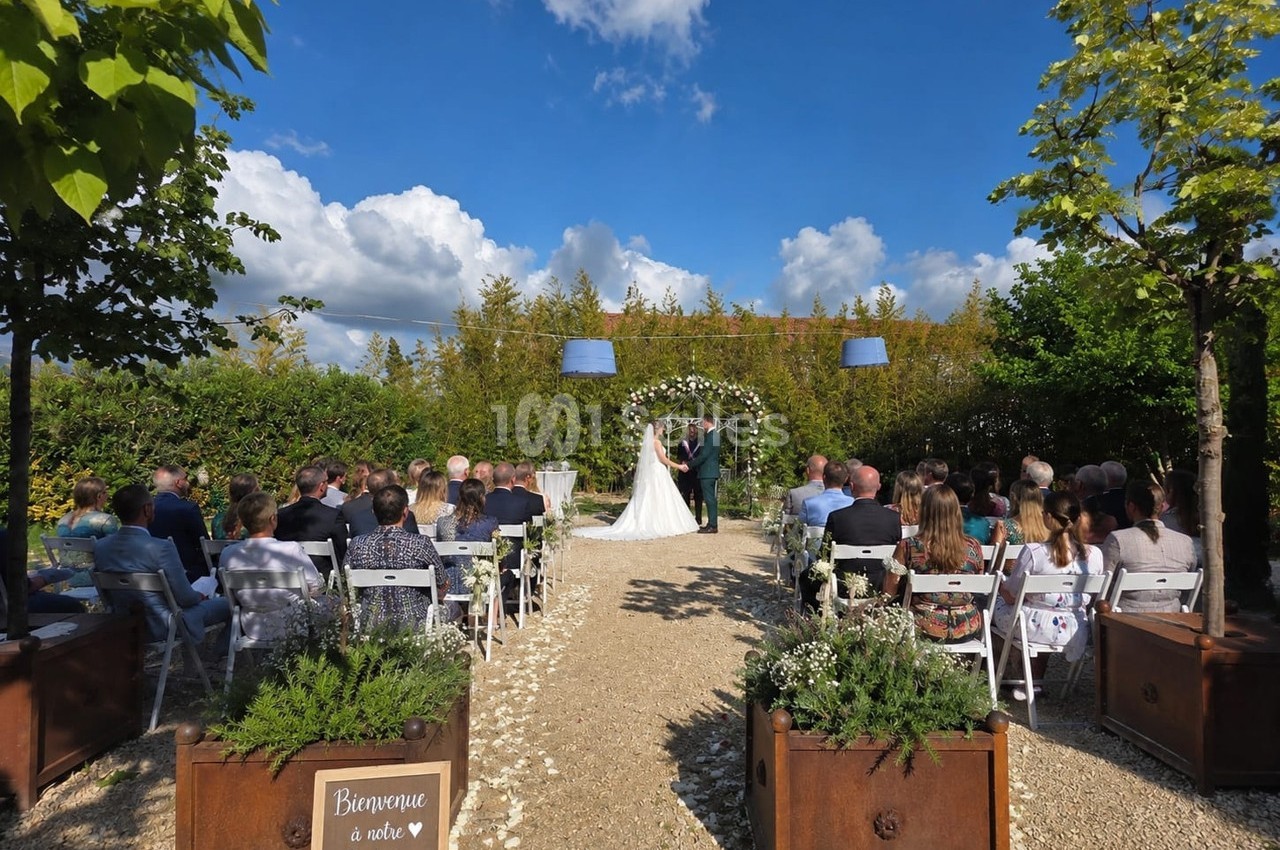 Mariage en extérieur avec des invités assis, un couple échangeant ses vœux sous une arche fleurie.