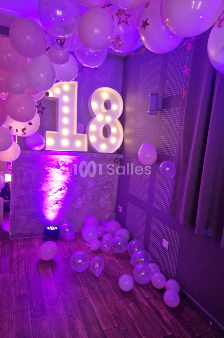 Décoration festive avec ballons roses et blancs, chiffres lumineux ’18’ et éclairage violet dans une pièce.