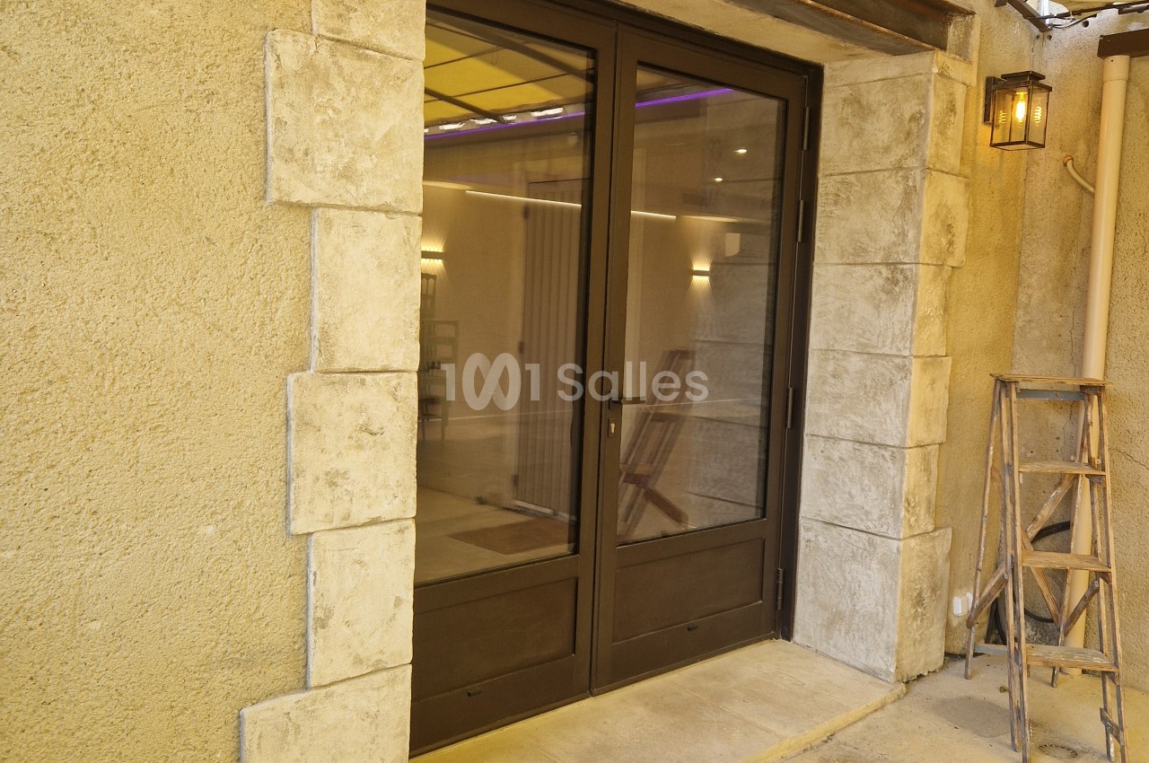 Entrée de salle avec double porte vitrée en bois, murs en pierre beige clair et éclairage intérieur tamisé.