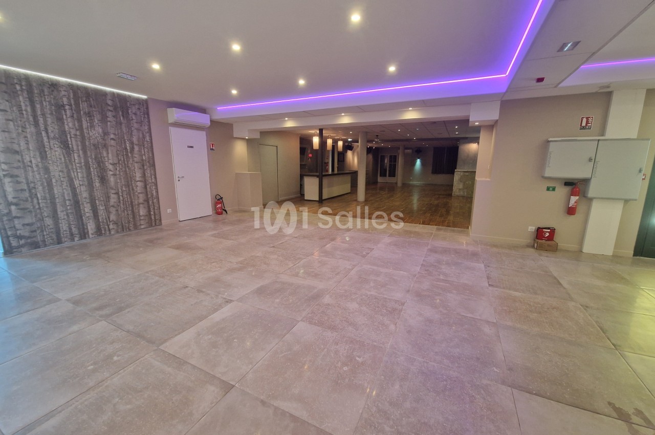 Salle intérieure vide avec sol carrelé beige, plafond blanc à néon violet, accueil au fond.