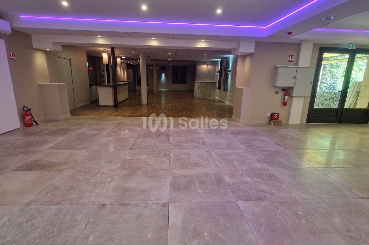 Salle vide au sol carrelé gris avec éclairage néon violet au plafond et accès à l'extérieur.