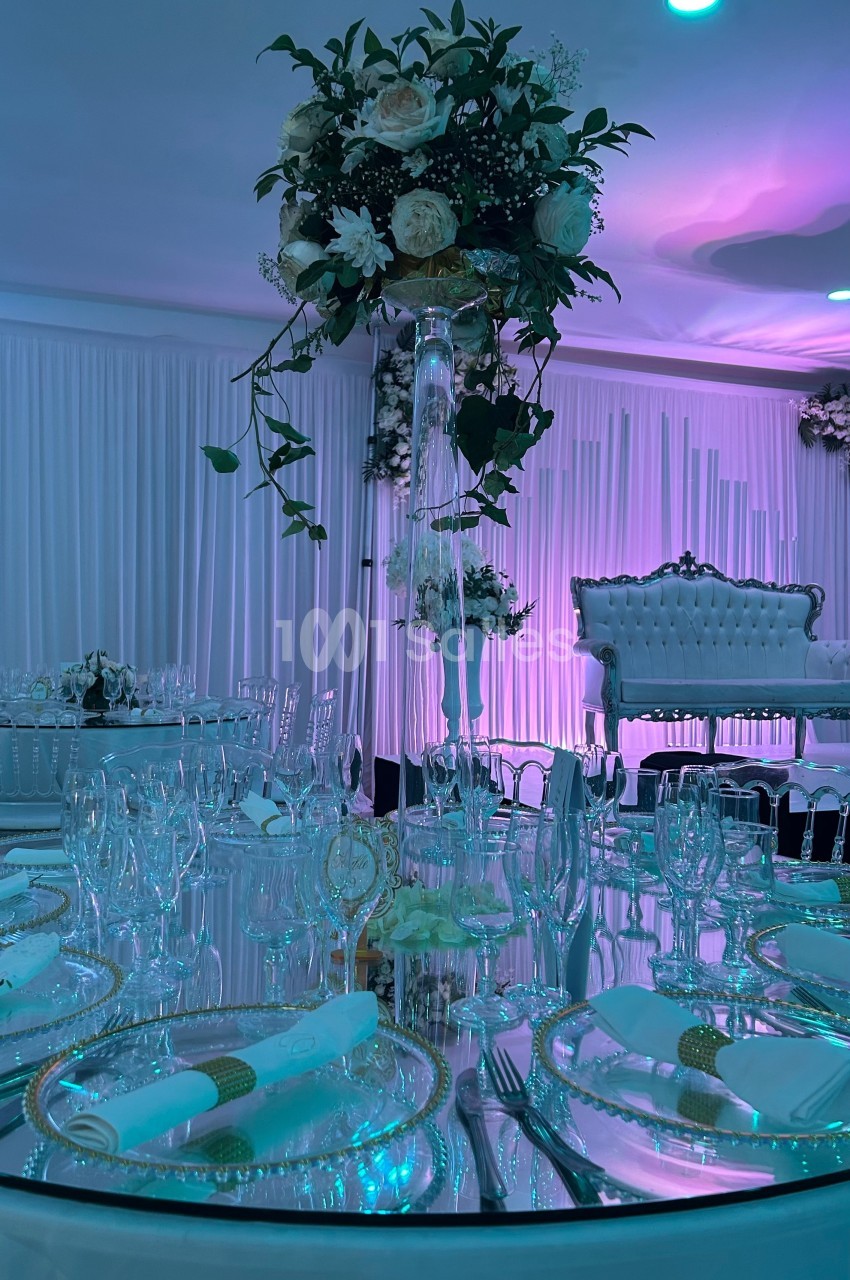 Table de réception élégamment dressée avec vaisselle raffinée, centre de table floral et éclairage tamisé violet.