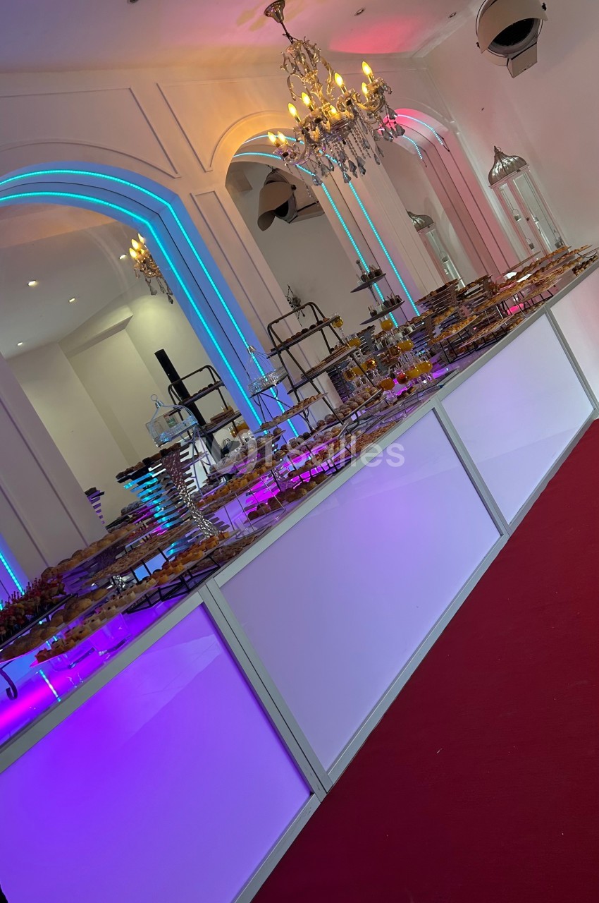 Buffet lumineux avec desserts variés disposés sur des présentoirs dans une salle décorée de lustres et d'arcs éclairés.
