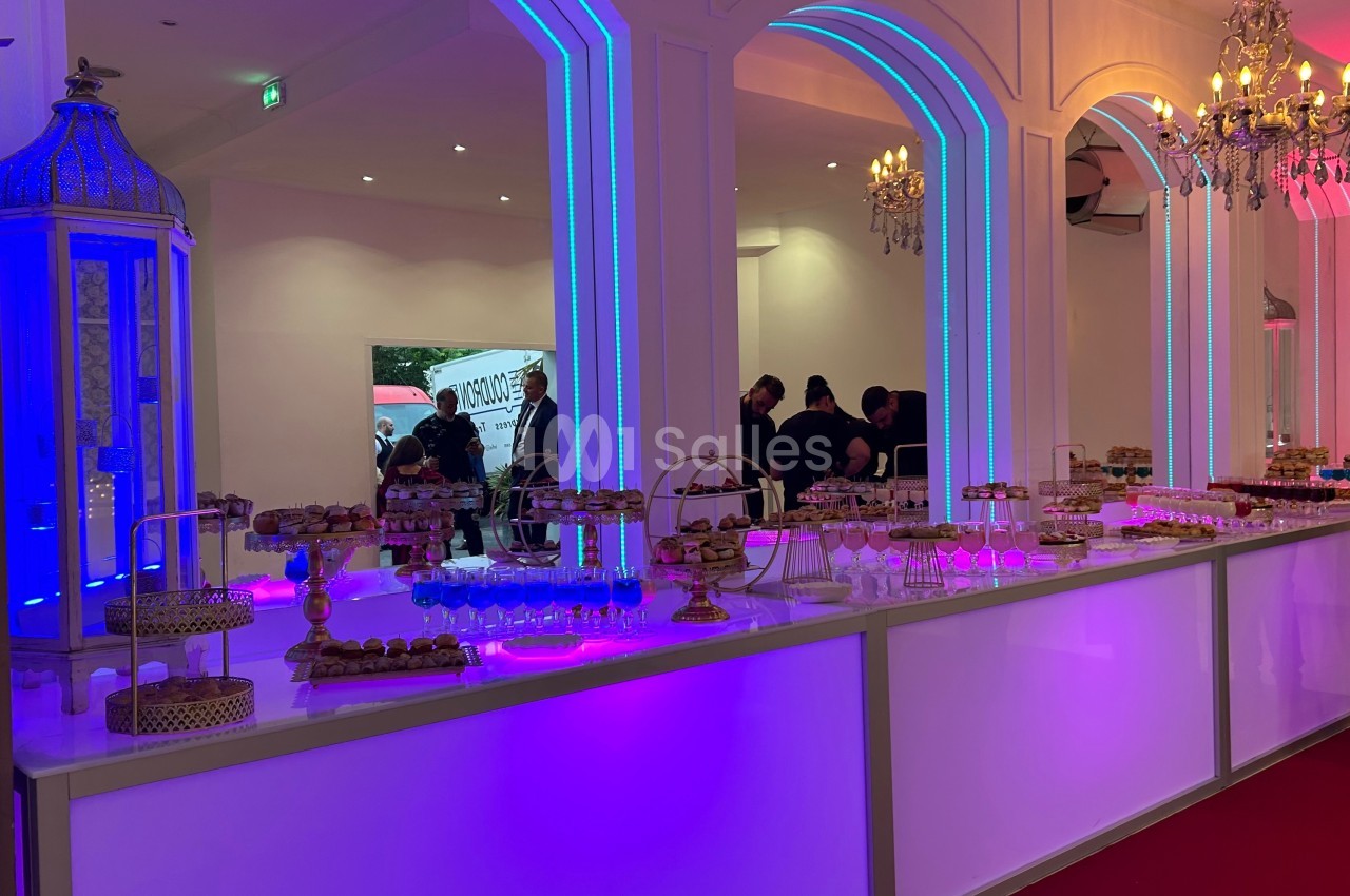 Buffet lumineux avec desserts variés présentés sur des supports élégants dans une salle décorée de lustres et d'arcs…