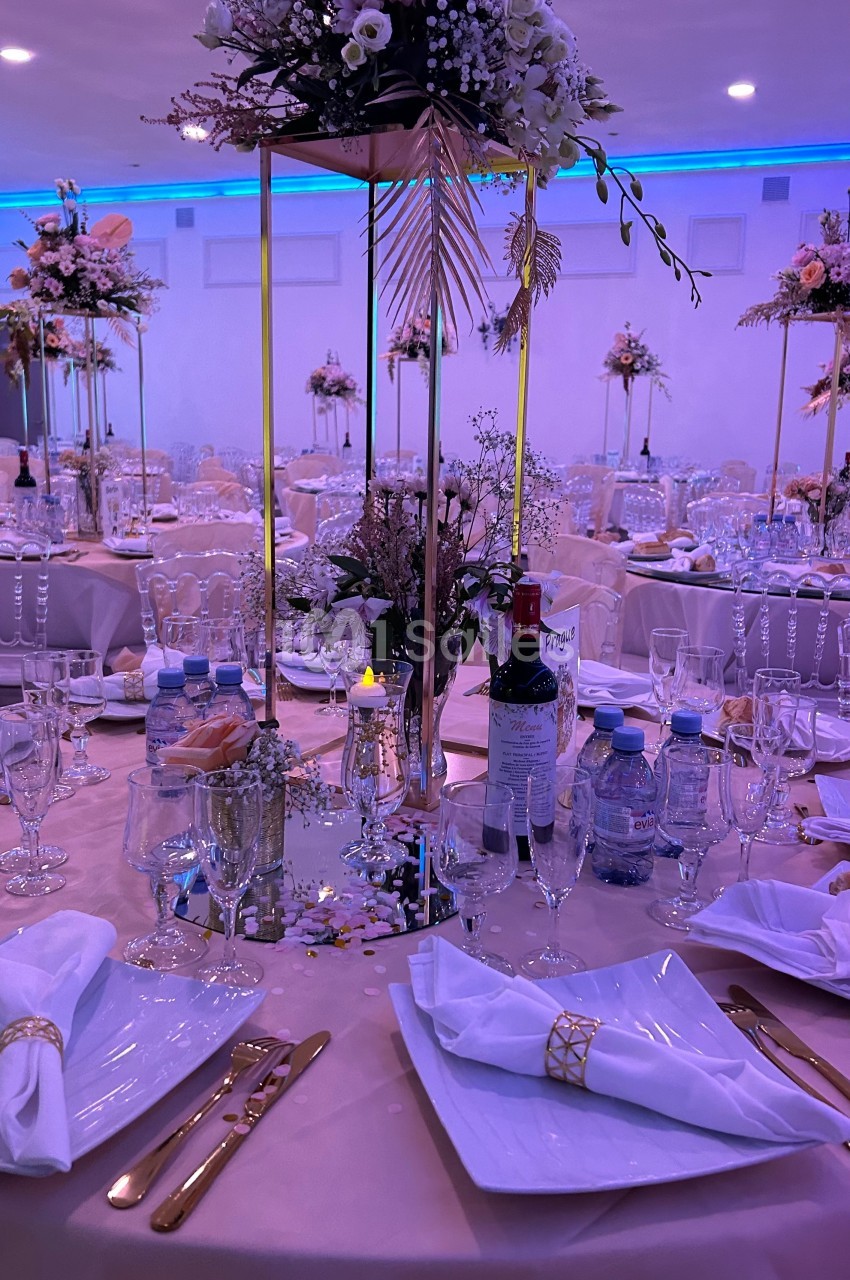Table de réception élégamment dressée avec nappes roses, décorations florales, couverts dorés et bouteilles sur la table.
