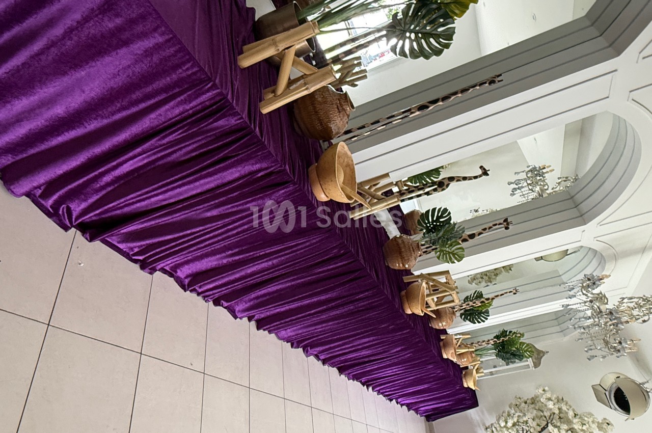 Table décorée d'une nappe violette avec des plantes, paniers en osier et éléments en bois, dans une salle lumineuse.