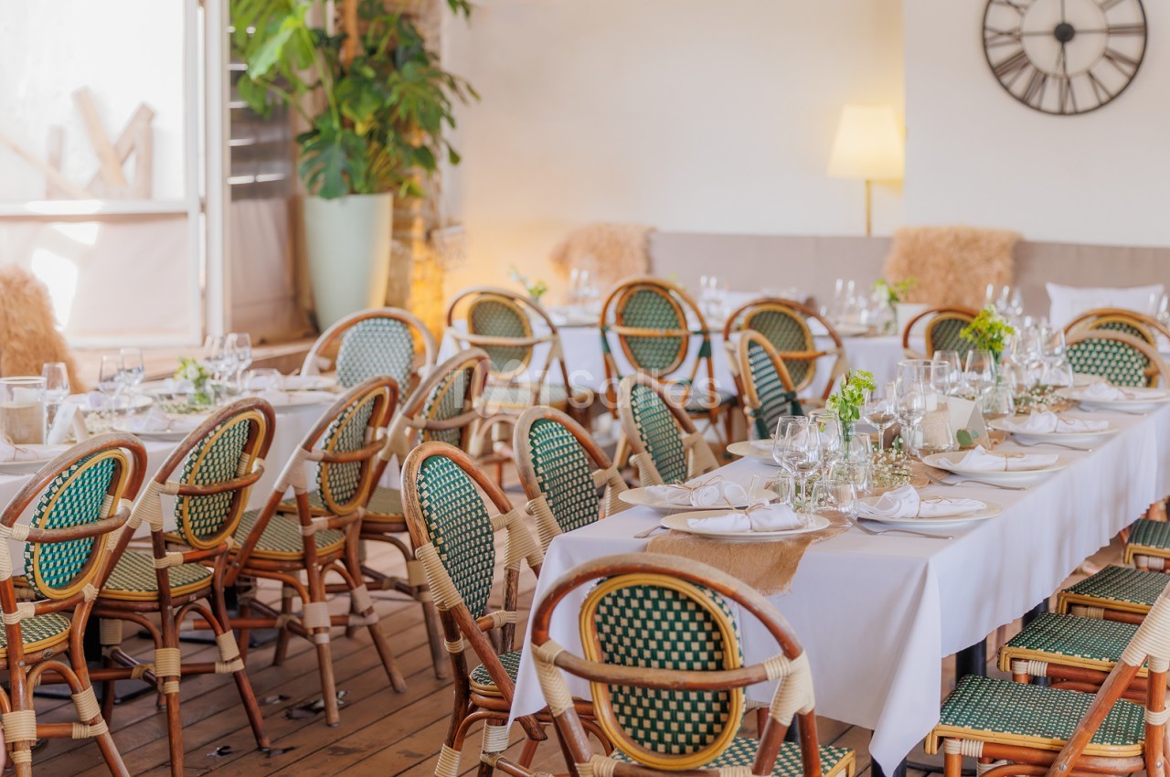 Salle de réception dressée avec chaises en rotin à dossier vert-jaune, tables blanches et verres - ambiance lumineuse et épurée.