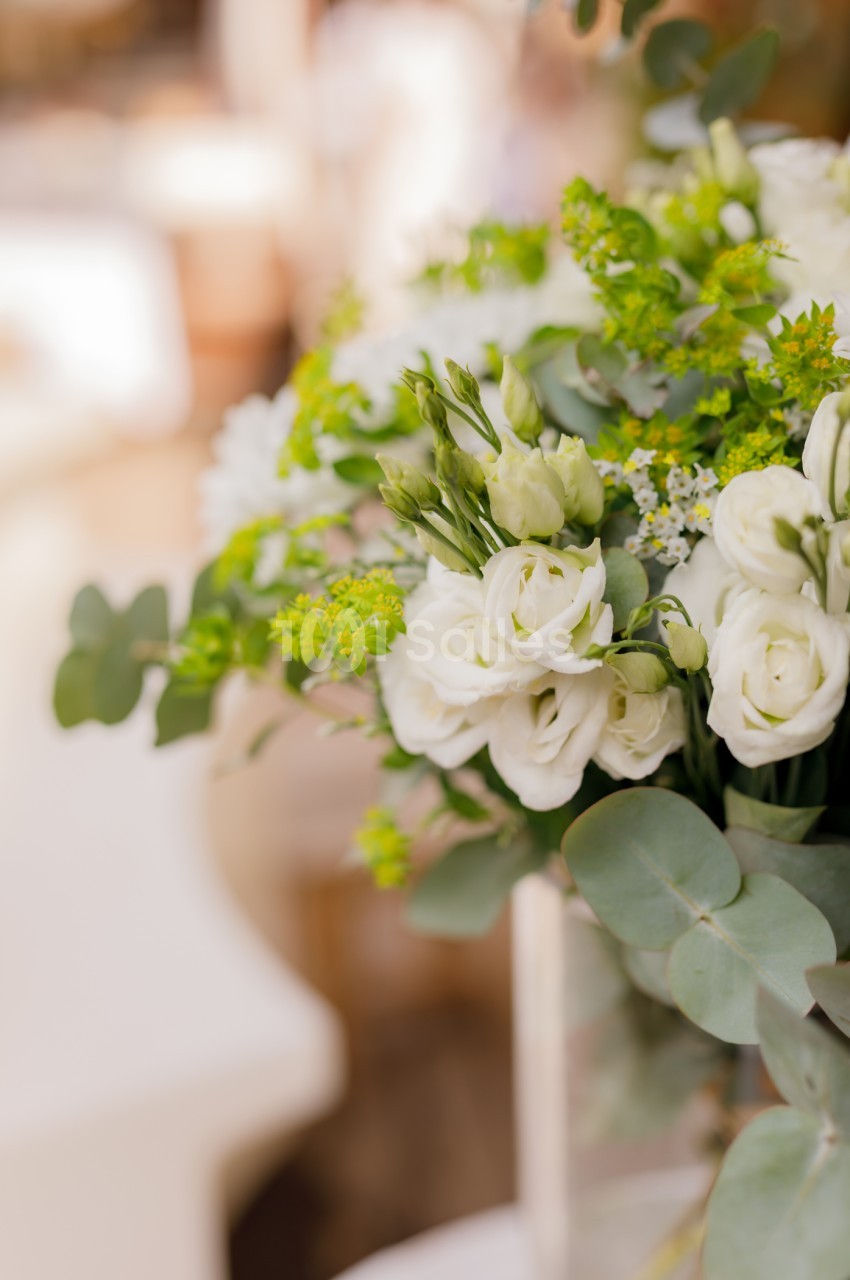 Bouquet de roses blanches et petites fleurs vertes avec feuillages dans un vase.