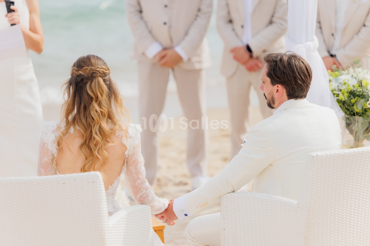 Cérémonie de mariage en bord de mer - mariés assis face à face, témoins en arrière-plan.