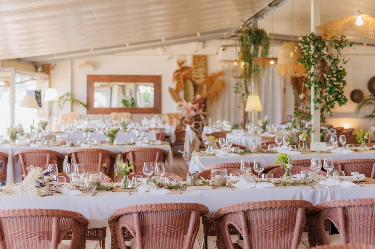 Salle de réception aménagée avec tables blanches, chaises en rotin rose et décoration florale minimaliste.