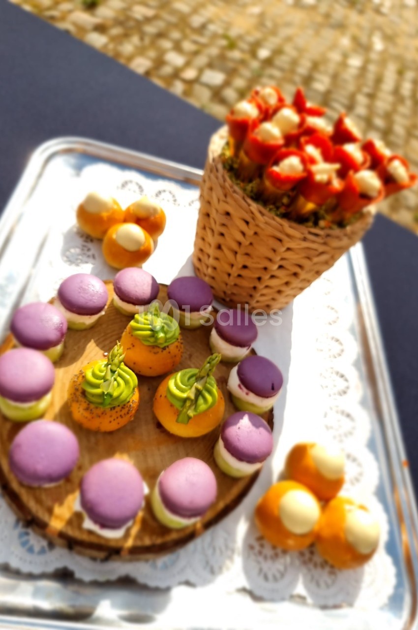 Plateau de pâtisseries colorées avec macarons violets, petits choux garnis et brochettes de fruits dans un panier.