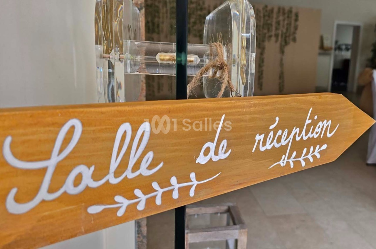 Panneau en bois indiquant ’Salle de réception’ avec une décoration végétale en arrière-plan.