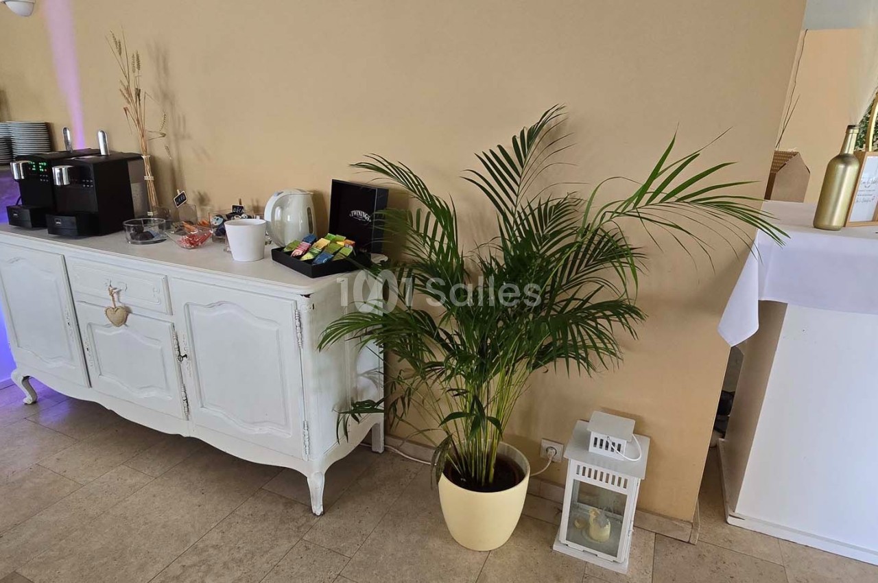 Buffet avec machine à café, tasses, capsules colorées, et une plante verte en pot à côté d'une lanterne blanche.