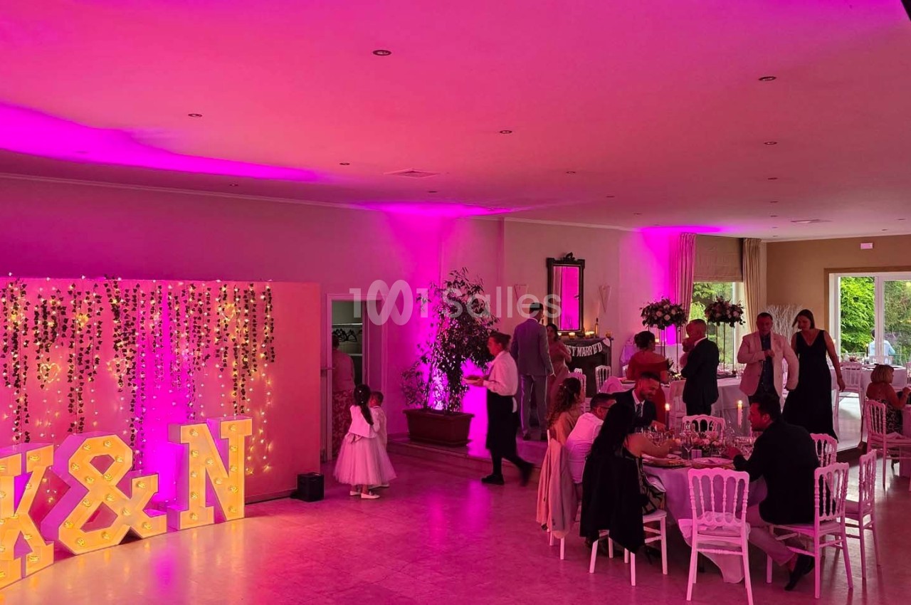 Salle de réception décorée avec des lumières roses, des invités assis et un mur illuminé avec les lettres ’K&N’.