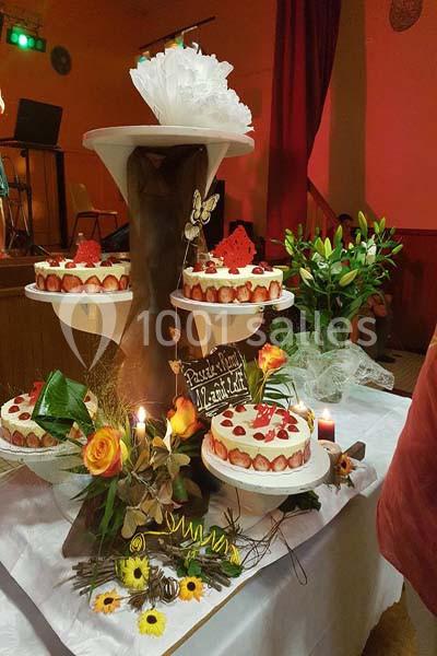 Présentoir avec trois gâteaux décorés de fraises et de crème, entouré de fleurs et de bougies sur une table.