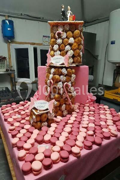 Pièce montée de choux et macarons roses sur une table décorée, avec figurines de mariage au sommet.