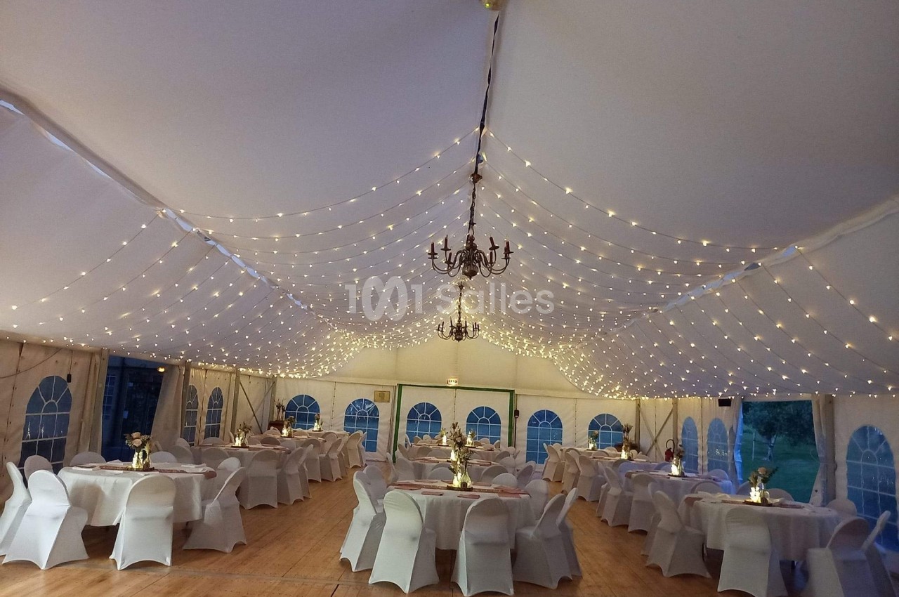Salle de réception sous chapiteau avec tables dressées et guirlandes lumineuses suspendues au plafond.
